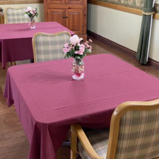 A dining room with tables covered in purple tablecloths, featuring floral centerpieces in vases.
