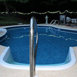 A serene outdoor swimming pool at night, illuminated by string lights.