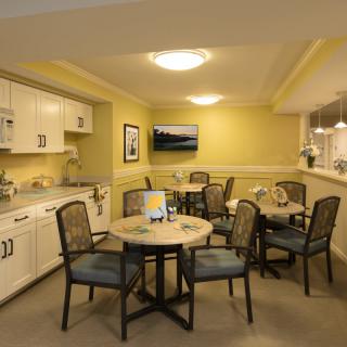 A cozy kitchen and dining area with round tables, comfortable chairs, and a mounted television.