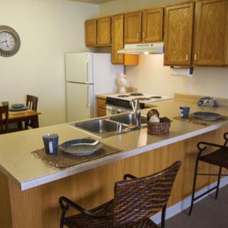 A cozy kitchen with a dining area, featuring wooden cabinets and a countertop with seating.