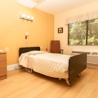 A simple and serene hospital room featuring a single bed, warm orange walls, and natural light filtering through the window.