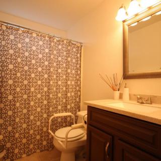 A cozy bathroom with a patterned shower curtain, wooden vanity, and warm lighting.