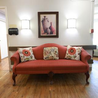 A cozy living room setup featuring a red sofa adorned with decorative pillows and framed artwork, illuminated by soft wall lights.