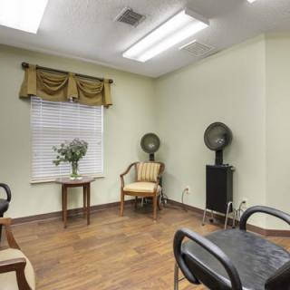 A cozy salon interior with chairs, hair dryers, and a decorative table near a window.