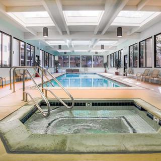 A serene indoor recreation area featuring a swimming pool and hot tub, with natural light streaming through skylights.