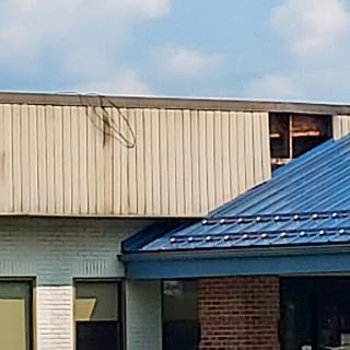 A view of a building with visible roof damage, featuring a contrasting blue roof against a cloudy sky.