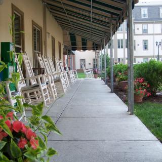 A covered porch with rocking chairs lined up alongside a building.