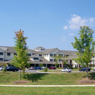 A suburban residential building with trees and parked cars on a sunny day.