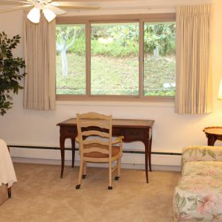 A cozy bedroom with a desk, chair, and large window overlooking greenery.