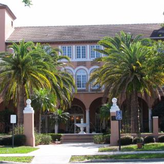 A building with arched windows and palm trees at the entrance, flanked by statues.