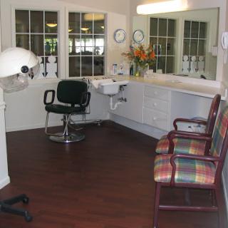 A cozy hair salon interior featuring a styling chair, waiting chairs, and natural light.