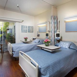 A well-lit hospital room with two patient beds, decorated with flowers and equipped with medical devices.