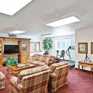A cozy living room with plaid sofas, a large TV, and exercise equipment near a window.