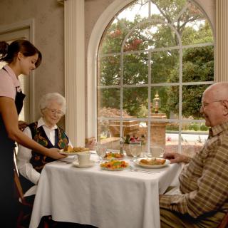 A waitress serving food to an elderly couple at a restaurant.