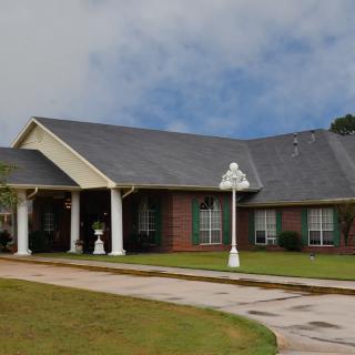 A single-story brick house with a neatly maintained yard and a driveway under a cloudy sky.