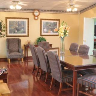 A well-furnished dining room with a large table and chairs, decorated with paintings and a vase of flowers.