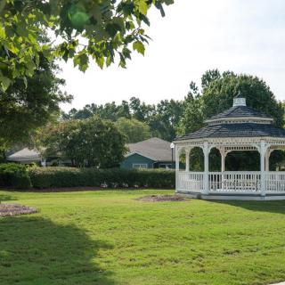 A serene park featuring a gazebo surrounded by a lush, green lawn and trees.