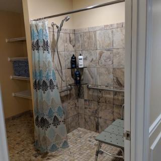 An accessible shower with a bench, tiled walls, and a patterned curtain.