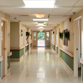 A clean and well-lit hospital hallway with several doors along the sides, featuring a simple decor.
