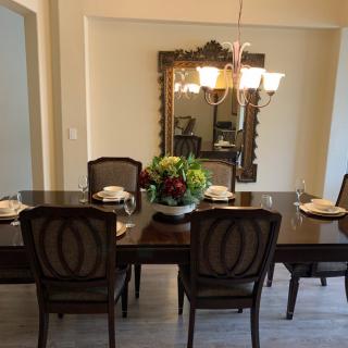 Elegant dining room with a dark wooden table set for a meal, complemented by a decorative mirror and chandelier.