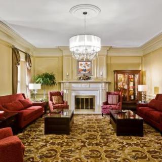 A traditionally decorated living room featuring plush, red sofas, a central chandelier, and an ornate fireplace.