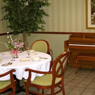 A dining area featuring a round table with chairs, set with floral decorations and a piano in the background.
