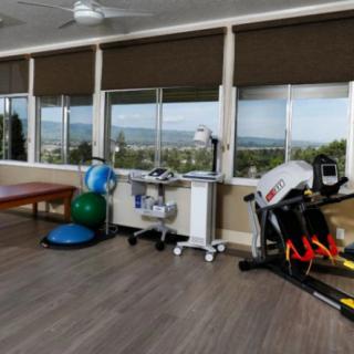 A bright gym with various exercise equipment and a scenic mountain view through large windows.