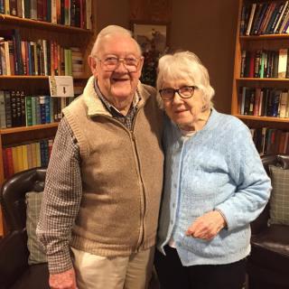 An elderly couple smiling together in front of a bookshelf.