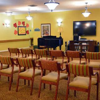 A well-arranged conference room featuring rows of chairs facing a piano and a television, with artwork on the walls.