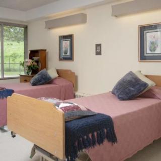 A well-lit bedroom with two single beds, each adorned with pillows and throws, features a large window and framed artwork on the walls.