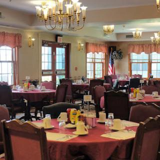 A cozy dining room set up for a meal, featuring red tablecloths and decorative chandeliers.