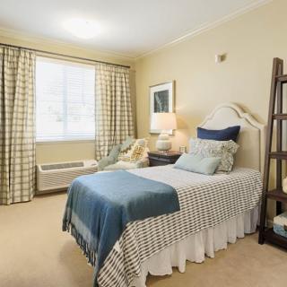 A cozy bedroom with a single bed, checkered curtains, and a bedside lamp.