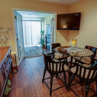 A cozy dining area with a round table and chairs, a mounted TV, and glass doors leading to another room with indoor plants.