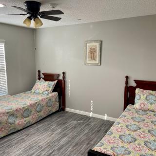 A cozy bedroom with two single beds, a ceiling fan, and simple decor.