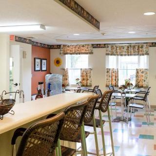 A cozy dining area with bar stools and tables, featuring large windows with floral curtains.