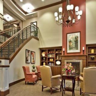A cozy living room featuring a chandelier, fireplace, and elegant staircase with bookshelves and comfortable seating.