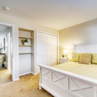 A cozy and well-lit bedroom with a white bed, decorative pillows, built-in shelves, and a bedside lamp.
