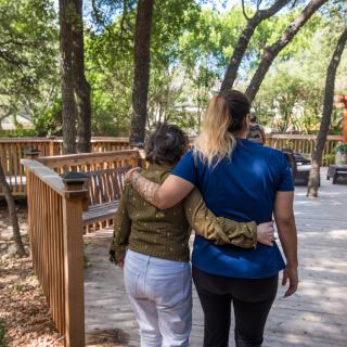 Two people walking arm in arm on a wooden path surrounded by trees.