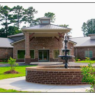 A brick building with a central entrance and a fountain in the foreground surrounded by well-maintained landscaping.