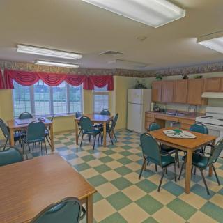 A communal kitchen and dining area with multiple tables and chairs, featuring large windows and a checkered floor.