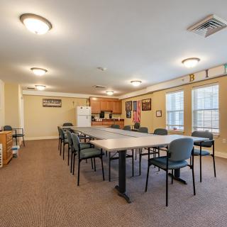 A spacious meeting room with a large conference table and chairs, adjacent to a small kitchen area.