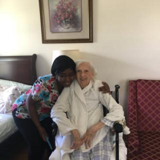 A caregiver affectionately hugs an elderly person sitting in a wheelchair.