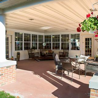 A cozy covered patio with outdoor furniture and hanging plants.