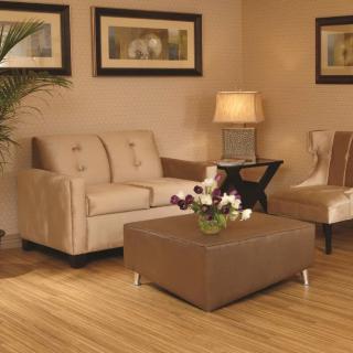 A cozy living room with a beige sofa, armchair, and ottoman, complemented by a lamp and wall art.