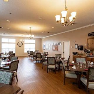 A well-lit dining room with neatly arranged tables and chairs, featuring elegant chandeliers and wooden flooring.