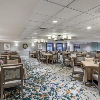 A spacious dining area with neatly arranged tables and chairs, elegant chandeliers, and a patterned carpet.