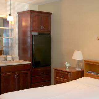 A cozy bedroom with wooden furniture including a cabinet and nightstand, featuring a comfortable bed and a lamp.