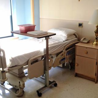 A hospital patient room featuring a bed, bedside table, and medical equipment.