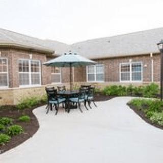 A cozy outdoor patio area with a table, chairs, and an umbrella surrounded by a landscaped garden.