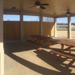 A spacious outdoor pavilion featuring picnic tables and ceiling fans, perfect for gatherings.